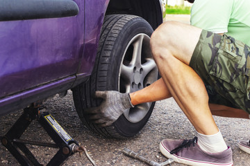 Obraz premium the man changes the tire in the car. pierce the wheels on the road.