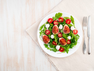 Fresh salad with figs, tomatoes, cucumbers, arugula, mozzarella. Oil with spices, top view, copy space, white background
