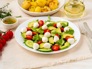 Fresh salad with tomatoes cucumbers arugula mozzarella and avocado. Oil with spices, baked potatoes, side view close up