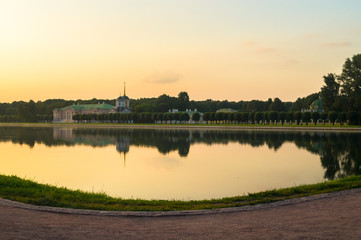 Fototapeta na wymiar Glossy mirror surface of palace pond in the sunset light. Ensemble of the State reserve museum Kuskovo, former aristocratic summer country estate of the 18th century. Moscow. Russia.