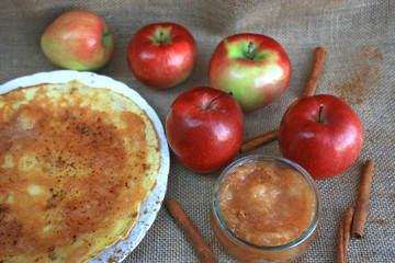 Apple marmalade with cinnamon in a jar, apples in the background, cinnamon sticks and pancake