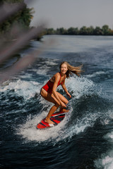 Sexy blonde woman wakesurfing on board down the blue water