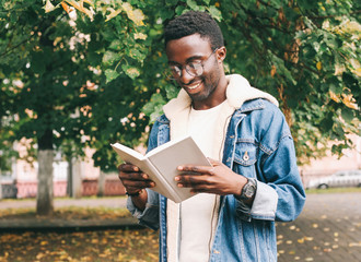 Happy smiling african man reading book in autumn city park