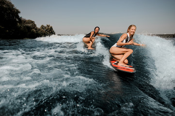 Two women wakesurfing on boards down the blue wave