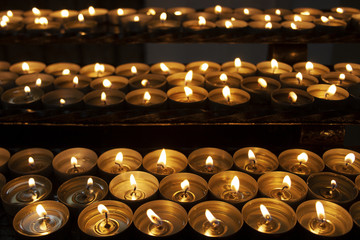 Many beautiful lit candles in a row glowing with a golden yellow light - selective focus