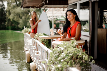 Two sexy women with wakeboard drinking champagne in outdoors restaurant