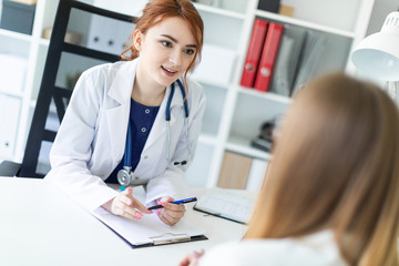 A beautiful young girl in a white robe is sitting at the desk in the office and communicating with...
