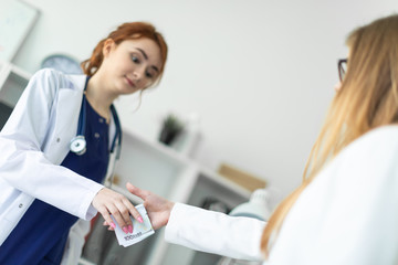 A beautiful young girl in a white robe is standing near a computer desk in the office and communicating with the interlocutor. The interlocutor shakes the girl's hand and hands her the money.