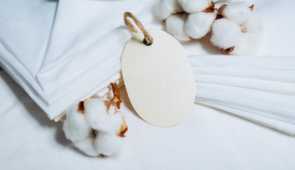 Close up oval paper tag beside pile of fabrics and cottons balls. Mock up cotton template on white.