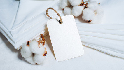 Close up rectangle paper tag beside pile of fabrics and cottons balls. Mock up cotton template on white.