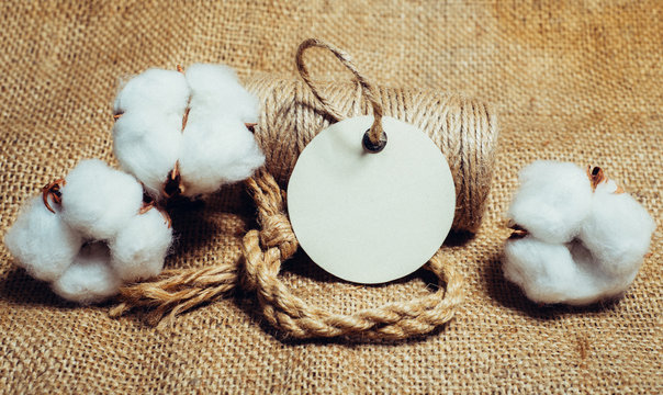 Close up round paper tag with rope on vintage fabrics beside cottons balls. Mock up cotton template on sackcloth.