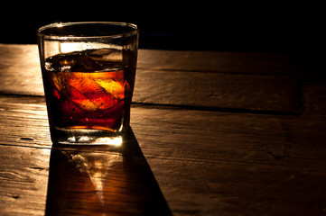 Cola with whiskey and ice on a wooden table background