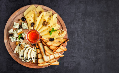 Cheese plate: Parmesan, cheddar, gouda, mozzarella and other with basil on wooden board on dark...