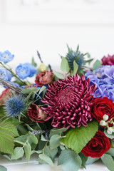 Elongated floral arrangement in vintage metal vase. table setting. Blue and red color. Gorgeous bouquet of different flowers. Bright room, stucco on the wall