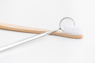 Closeup of mouth mirror next to simple wooden toothbrush on white background, dentistry and teeth care concept