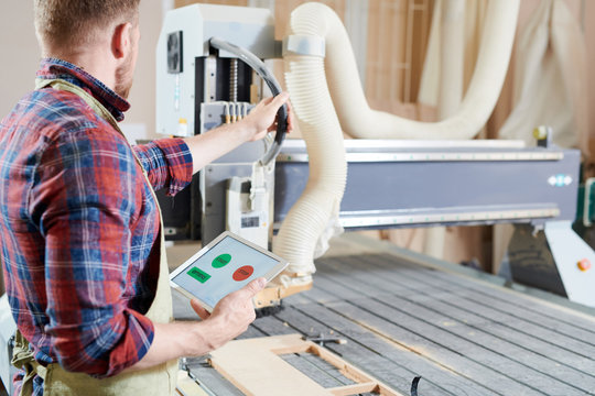 Young operator using digital tablet while working on machine in workshop
