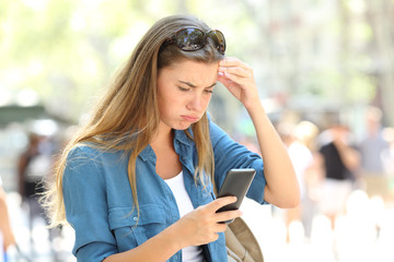 Frustrated woman reading phone content in the street