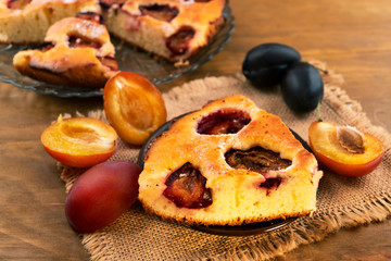 A delicious dessert is a pie baked in the oven with plums, whole and cut plums of lilac and blue color on a linen cloth.