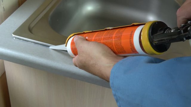 Plumber worker fix sealing washbasin with transparent silicone sealant in kitchen