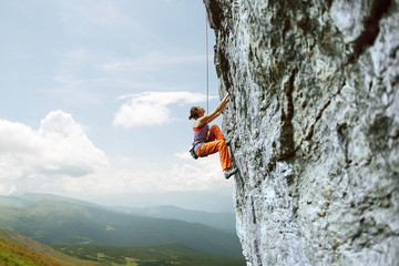 young slim female rock climber climbing on the cliff
