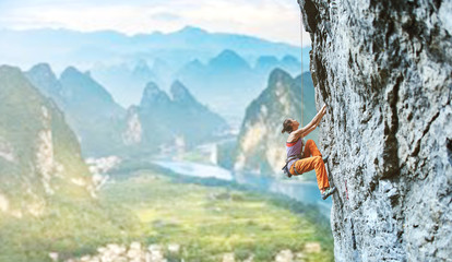 young slim female rock climber climbing on the cliff