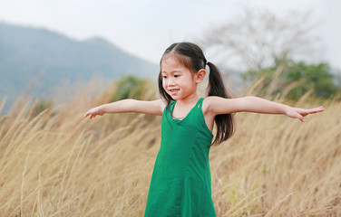 Adorable little Asian child girl with open arms in the dried grass field.