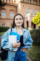 Fototapeta premium Happy young asian female student at college campus and carrying books