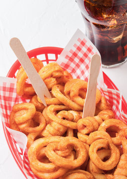 Curly fries fast food snack in red plastic tray with glass of cola on stone kitchen background. Unhealthy junk food