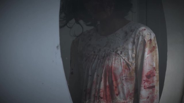 Scary ghost girl with bloody clothes in the mirror at dark night. Halloween concept. Shot in 4k resolution