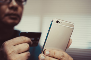 Asian man holding credit card and smart phone to shopping online