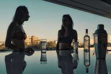 young woman enjoying a drink at a rooftop bar with a man preparing some cocktails