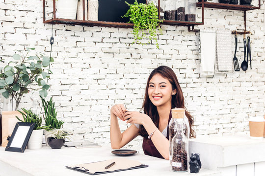 Portrait of woman barista small business owner smiling and holding cup of coffee behind the counter bar in a cafe