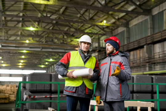 Waist up portrait of two industrial workers wearing warm jackets and hardhats discussing production standing in workshop, copy space