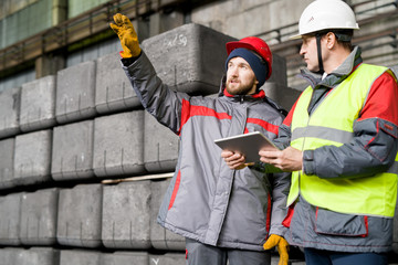Waist up portrait of modern bearded worker  wearing warm jacket and hardhat pointing up while...