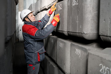 Side view portrait of mature factory worker wearing hardhat marking concrete blocks in industrial warehouse, copy space