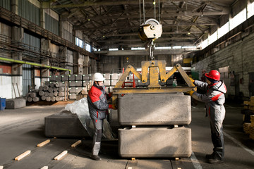 Full length side view portrait of two factory workers moving loads while using crane in workshop, copy space