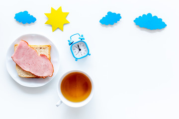 Parts of day. Morning. Time for breakfast. Tea, sandwich near alarm clock, sun and clouds cutout on white background top view copy space