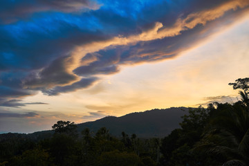 Dramatic clouds against the backdrop of mountains at sunset on a tropical island.
