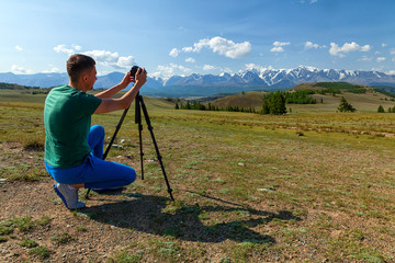 Travel  hiking man shoooting  mountain landscape. Tourist professional photographer on  vacation shooting,   camera on tripod.