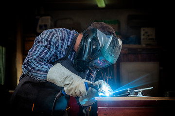 A strong man welder in a black T-shirt, in a welding mask and welders leathers weld metal welding...