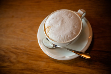 Cappuchino or latte coffe in a white cup with foam on wooden board. Morning energy drink isolated on dark wooden background. Copy space. Top view. Hot drinks.Good morning concept