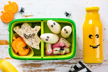 Halloween style school lunch box - ghost sandwich, pumpkin carrots, bananas, juice, top view
