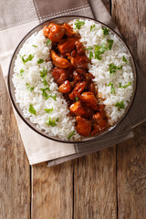 Stewed Bourbon chicken in sauce with whiskey, sugar, ginger and soy, served with rice on a plate. Vertical top view
