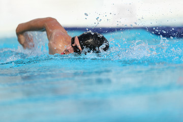 Obraz na płótnie Canvas Swimming pool athlete training indoors for professional competition. Swimmer man on swim practice in stadium doing crawl with arm splashing water. Copy space on blue water background.
