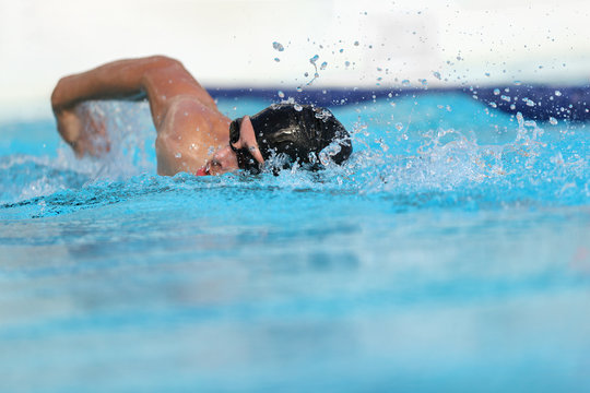 Swimming pool athlete training indoors for professional competition. Swimmer man on swim practice in stadium doing crawl with arm splashing water. Copy space on blue water background.