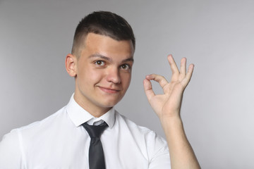 Happy young man in shirt and tie gesturing OK sign and smiling