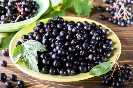 Ripe black chokeberry  in bowl and branch of aronia  on rustic wooden background