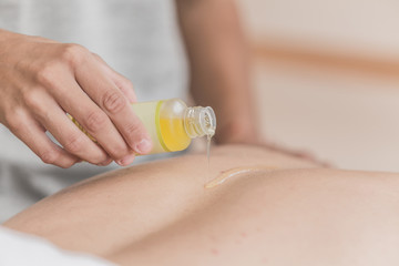 Masseuse pouring masage oil on the bod. close-up