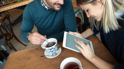 Young attractive couple having fun with tablet in cafe