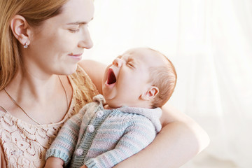 Pretty woman holding  yawning newborn baby in her arms. Close up image. Motherhood concept. Happy family concept